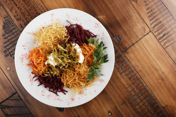 Chafan (Azerbaijan kitchen), mix from potato, carrot, beet, greens on white plate. wooden background