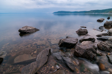 Small creek flow into smooth surface of Baikal lake. Big stones and pebbles seen through clear...