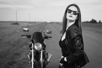 Fototapeta na wymiar Biker girl in a leather jacket posing near motorcycle