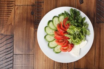 vegetable mix (salad, cucumber, tomato, parsley) and chees on a white plate. wooden background.