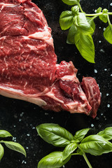 Fresh steak served with spices, tomatoes and leafs of basil on marble background. Uncooked beefsteak cooking on a kitchen. Delicious, spicy, juicy meat with copy space closeup.
