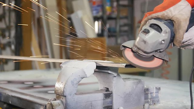 worker grinding a steel metal bar with angle grinder in workshop close up