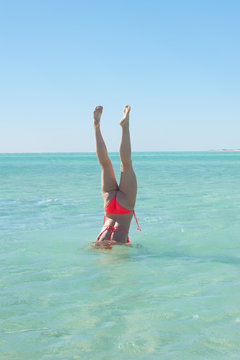 Sporty bikini woman handstand ocean water