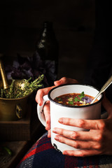Mug with soup in female hands.