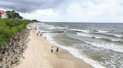 Ustronie Morskie na Pomorzu Zachodnim - ludzie spacerujący po plaży w letni, pochmurny dzień - obrazy, fototapety, plakaty