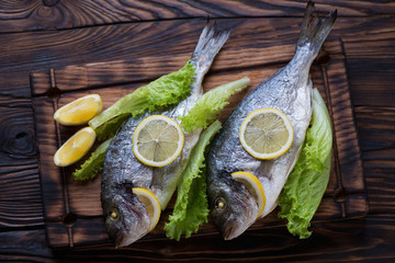 Two baked doradoes with green salad and lemon on a serving board
