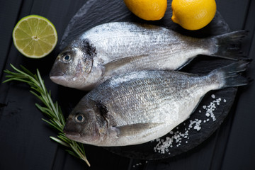 Fresh uncooked doradoes with condiments on a stone slate tray