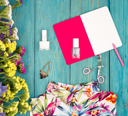 dress, colorful flowers, cosmetics makeup, notepad, bijou and essentials on blue wooden background