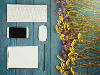 slim keyboard, mouse, smart phone, notepad, colorful flowers on blue wooden desk