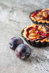 Homemade cake tartlets with plum on old stone background