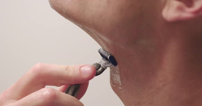 Man shaving with a wet razor and foam to remove stubble on chin.  Slow motion recorded at 60fps, extreme close up, profile.