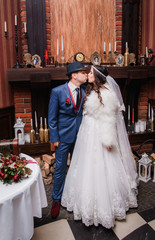 Bride in white fur coat kisses a groom in blue suit standing bef