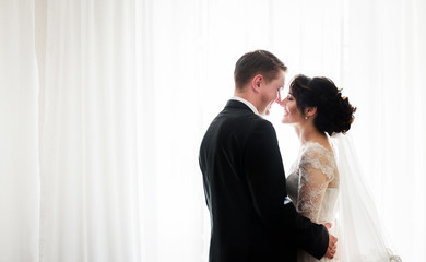 Happy wedding couple stands smiling before white large window