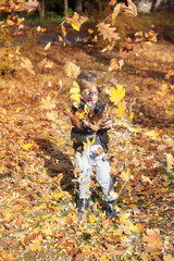 Happy kid playing in park and throwing yellow leaves. Excited boy throwing autumn leaves.
