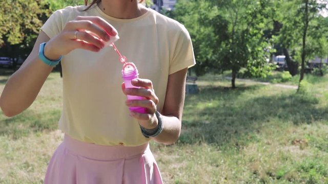 Girl in a yellow T-shirt and pink skirt blowing bubbles in the park in the summer