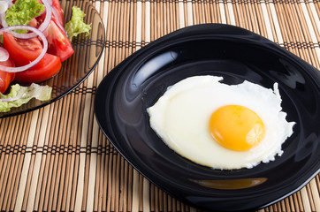 Close-up top view on a black plate with a fried egg