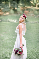 Fototapeta na wymiar Chic young bride in red wreathe poses in the garden holding red