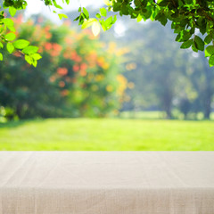 Naklejka na ściany i meble Empty table with linen tablecloth over blur park background