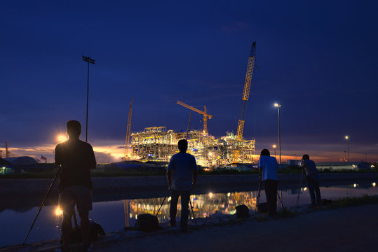 Landscape photographers shooting images photography at construction oil and gas rig plant at twilight.