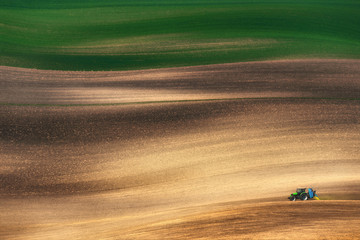 Farming tractor plowing and spraying on field. Small blue tractor working on a colorful spring field.Agriculture tractor cultivating field and creating abstract background texture - 118902020