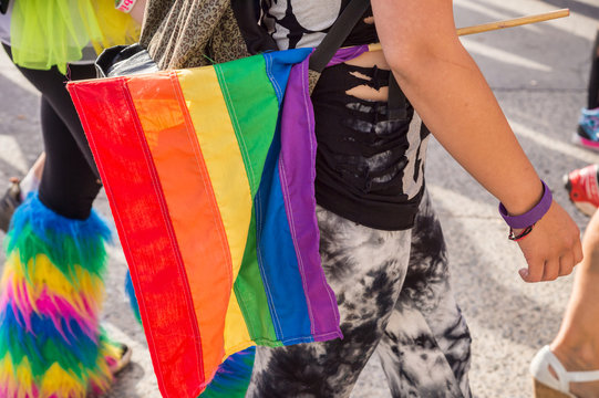Side view of a walking girl holding a gay rainbow gay flag 