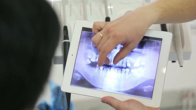 Dentist shows a radiograph of a patient using a tablet with a touchscreen.