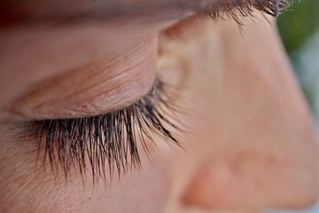 Macro detail of a closed woman eye with extremely long black natural eyelashes and dark brown eyebrows behind the thick sunglasses 