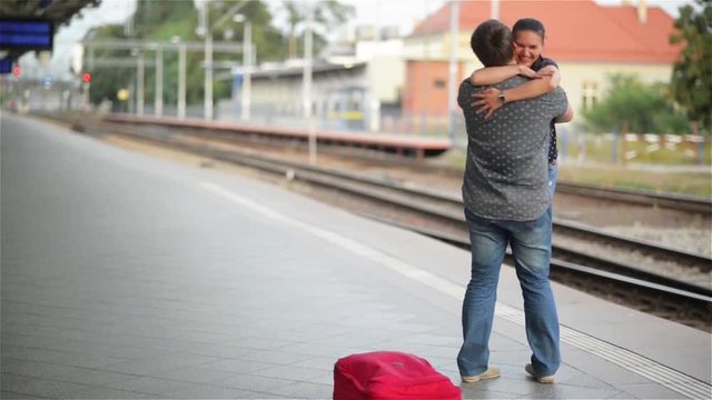 Young couple happy to meet again in the train station, girl runs to meet her boyfriend and throws a suitcase, twist on hands