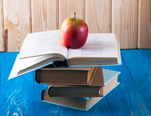 Stack of books and apple on a blue wooden shelf