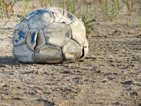 Balón de fútbol desinflado y roto sobre campo abandonado