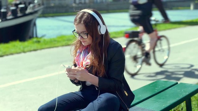 Pretty girl listening music on headphones and browsing internet on smartphone
