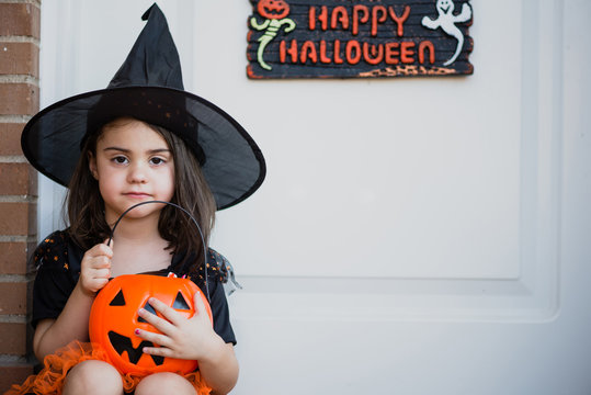 Pretty little girl in witch hat with pumpkin bag looking at camera