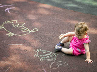 Naklejka premium Little girl draws a chalk on the playground