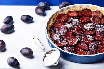 Homemade pie with plums and sieve on the table