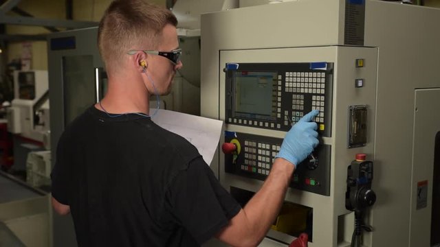 man programming a cnc machine and reading technical drawing