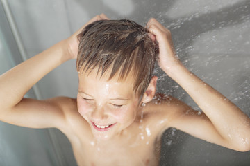 Happy teen boy washing head in shower in the bathroom
