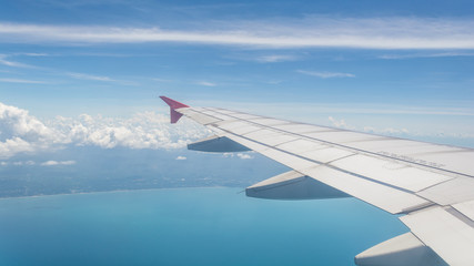Fototapeta premium Wing of a plane from window view with bright blue sky and sea background.