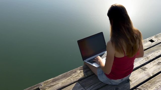 A young woman with laptop sitting on jetty