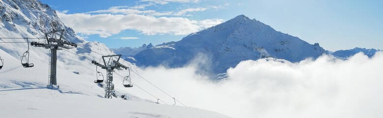 Winter mountains view with ski lift in the foreground and clouds in the valley. Corvatsch, Engadin, Switzerland.