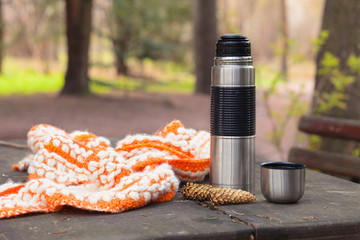 thermos and scarf on wooden table with nature on background. Tou