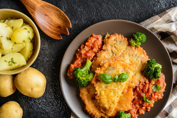 Piccata - fried pork cutlets stuffed with smoked ham slices coated in cheese and eggs served with tomato sauce, steamed broccoli and boiled potatoes