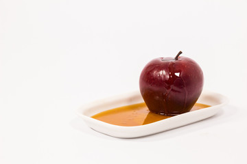 Red apple with drops of honey on white plate with honey isolated on a white background