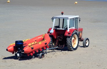 roter Traktor mit Motorschlauchboot auf einem Trailer am Sandstrand