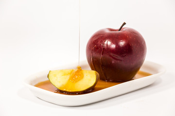 Pouring honey on red apple and red apple slice on white plate with honey isolated on a white background
