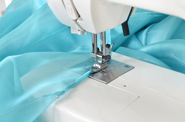 Sewing machine. Sewing process, hemming and stitching of edge of a stylish blue dress or tulle curtains