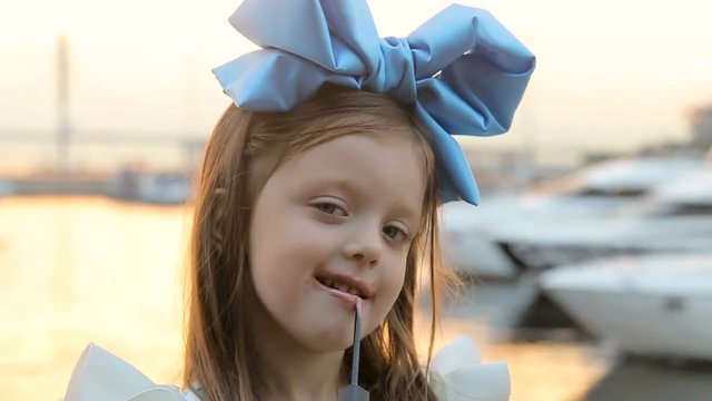 portrait of a little girl three years with the blue bow on her head, stands near the water