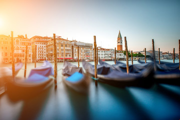 Venice cityscape view on Grand canal with colorful buildings, gondolas and San Marco campanille at the sunset. Long exposure image technic with motion blurred boats and glossy water - obrazy, fototapety, plakaty