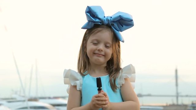 portrait of a little girl three years with the blue bow on her head, stands near the water