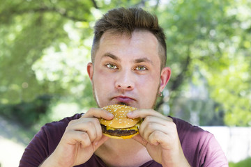 emotional young guy eating a cheeseburger on the nature