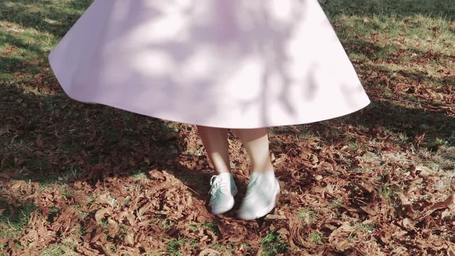 Girl in a pink skirt and blue shoes spinning in slow motion in the park on dry leaves
